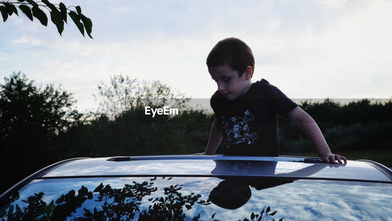 Boy standing and looking through car roof against sky