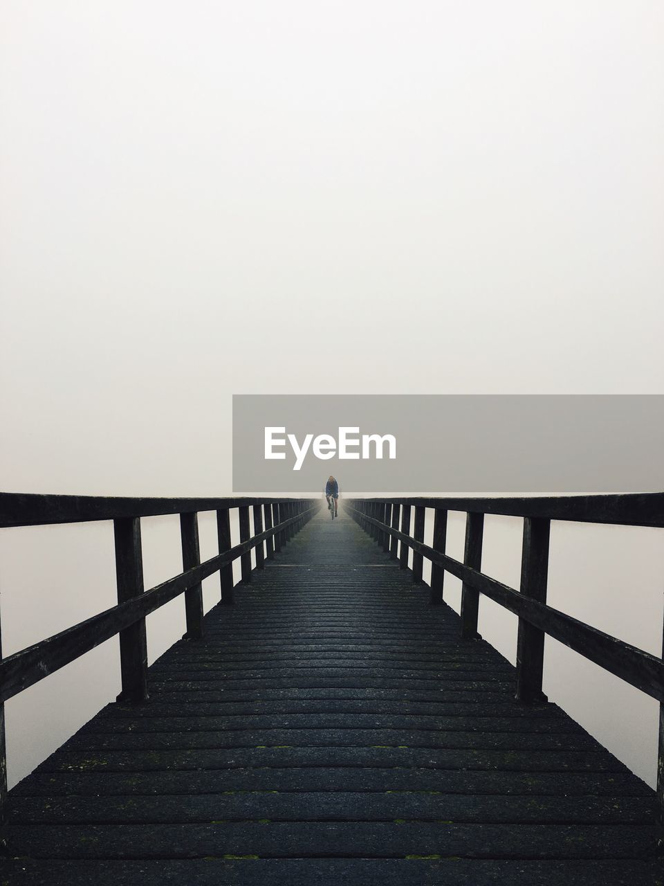 Person riding bicycle on footbridge against clear sky