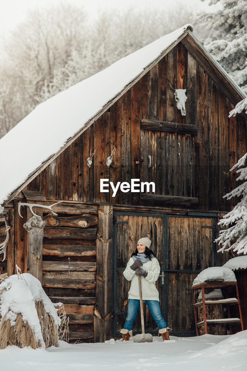 Smiling young woman standing on snow field by cottage