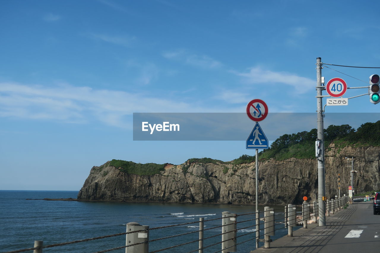 Road sign by sea against sky