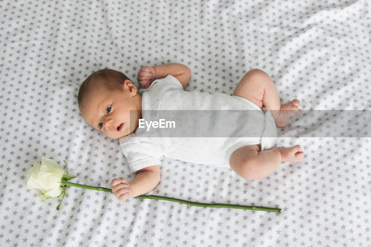 High angle view of baby with flower lying on bed