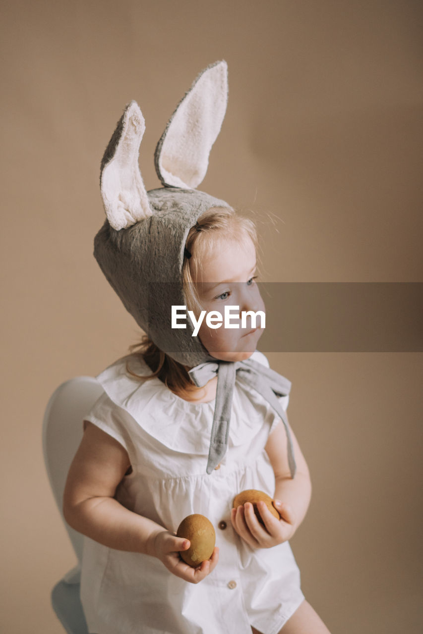 Toddler baby girl in funny hat with ears sitting with eggs in her hand