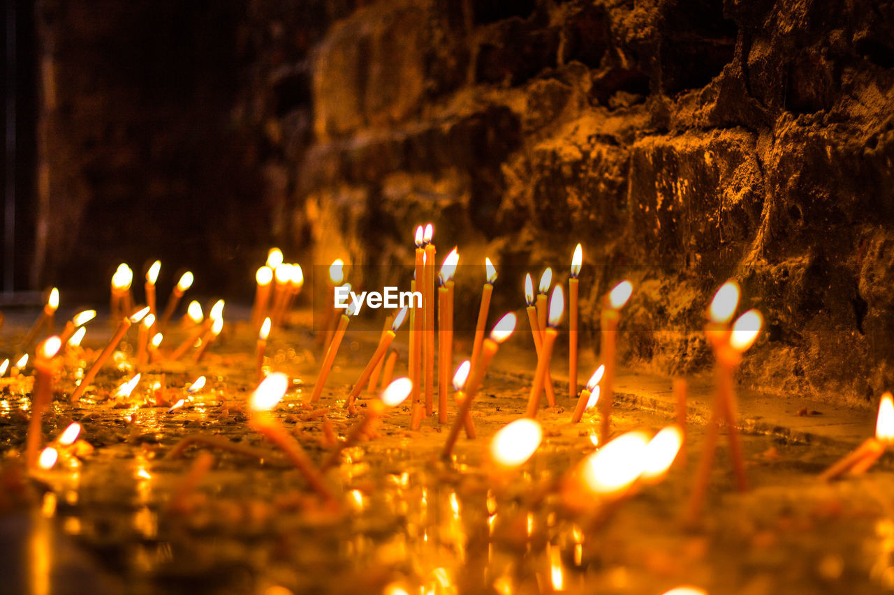 Close-up of burning candles by wall at night