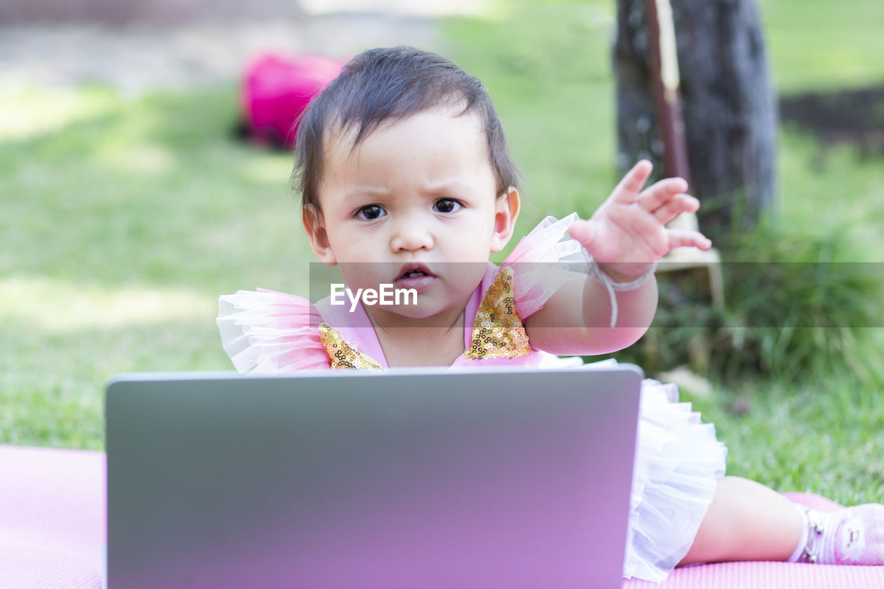 PORTRAIT OF CUTE GIRL LOOKING AT CAMERA WHILE SITTING ON MOBILE PHONE OUTDOORS