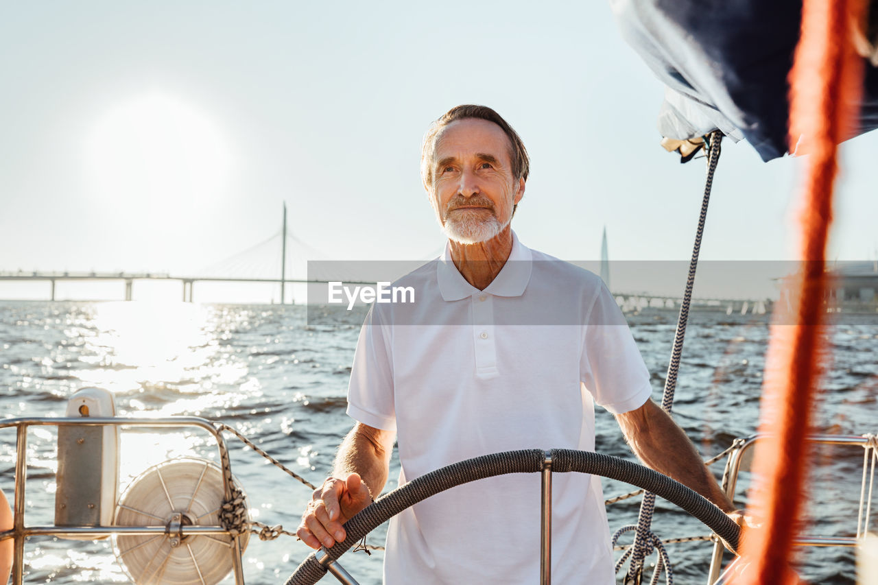 Senior man standing in sailboat against sky