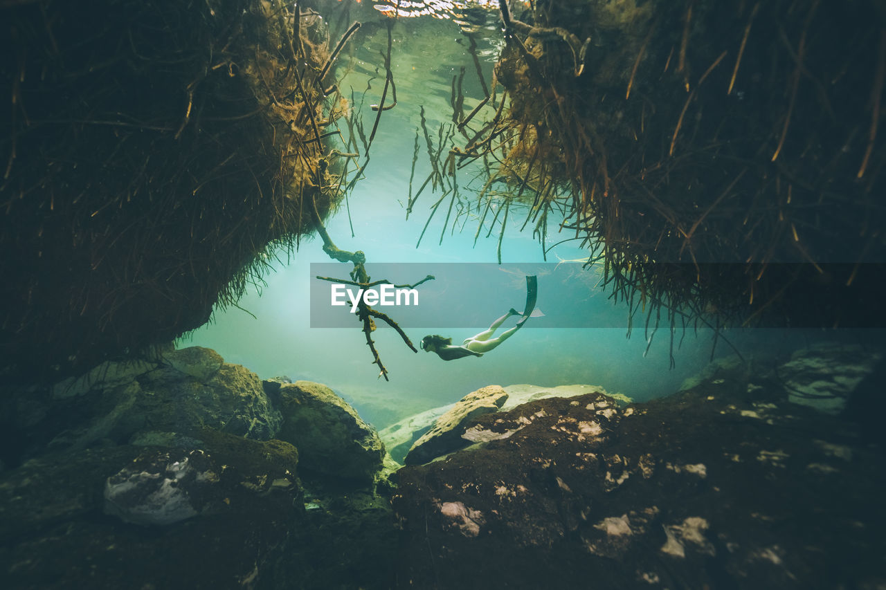 Woman swimming underwater by rock formation 