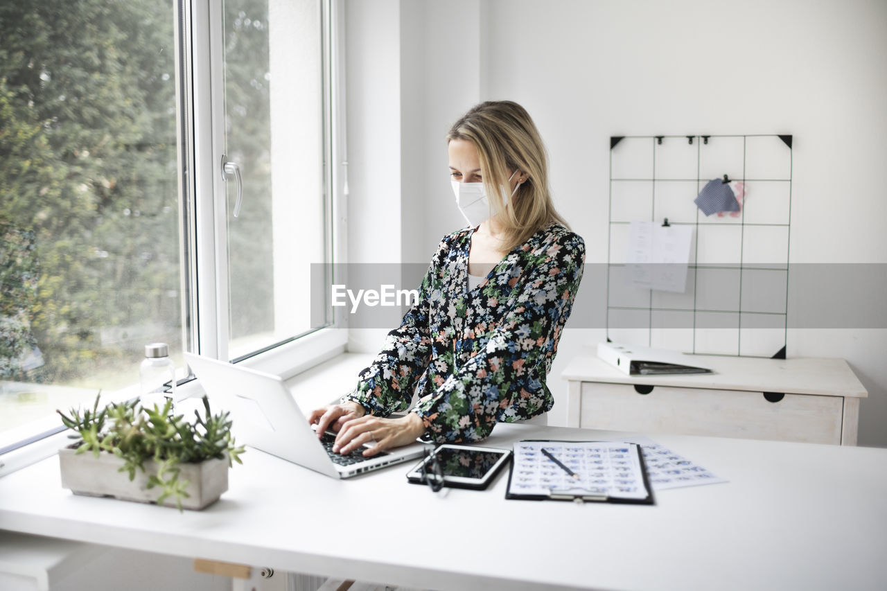 Businesswoman wearing mask using laptop at home