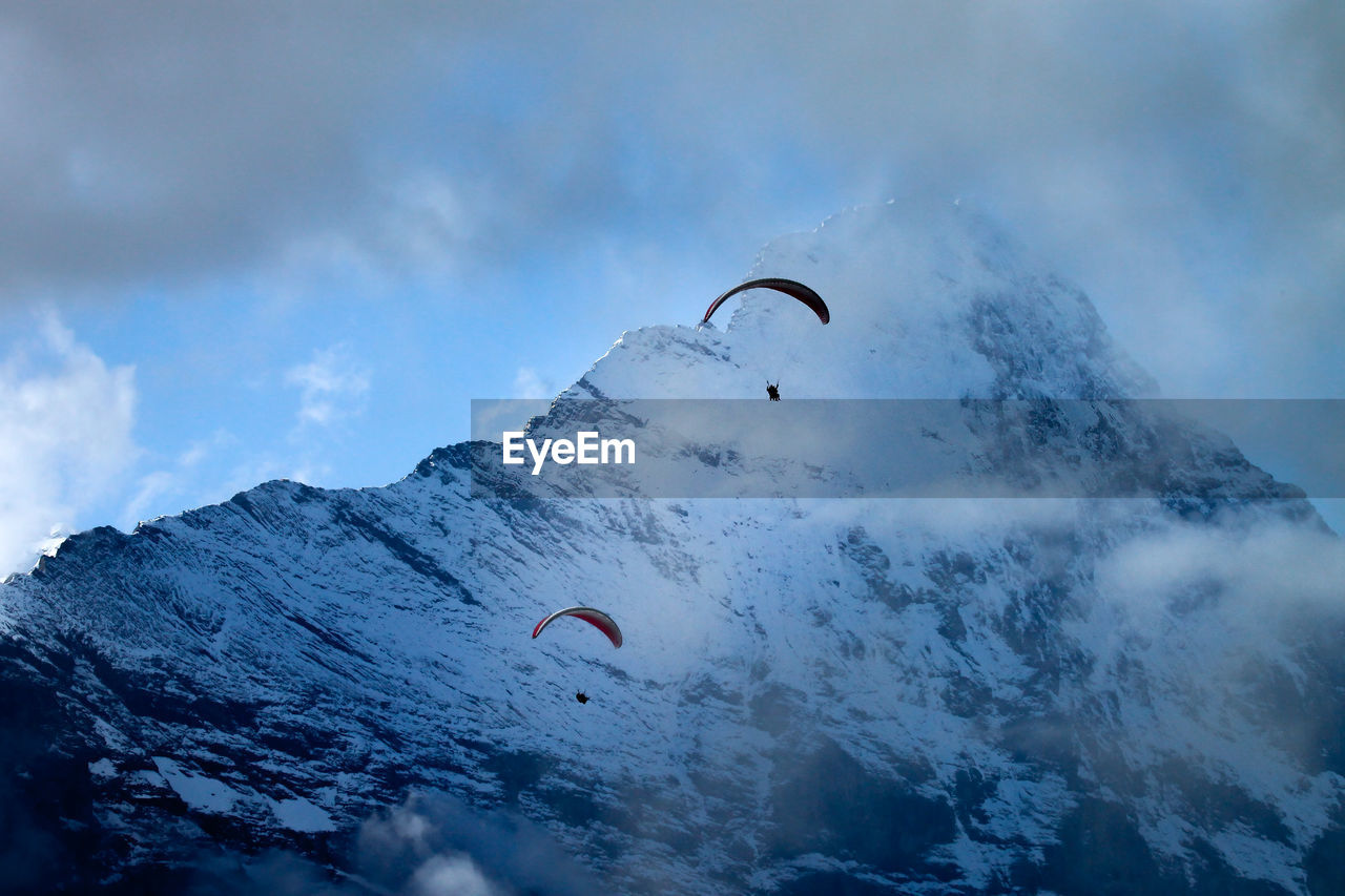 LOW ANGLE VIEW OF PERSON PARAGLIDING AGAINST MOUNTAINS
