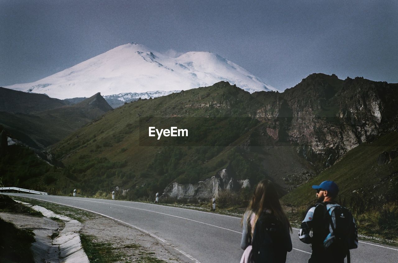 PEOPLE ON SNOWCAPPED MOUNTAIN ROAD AGAINST SKY