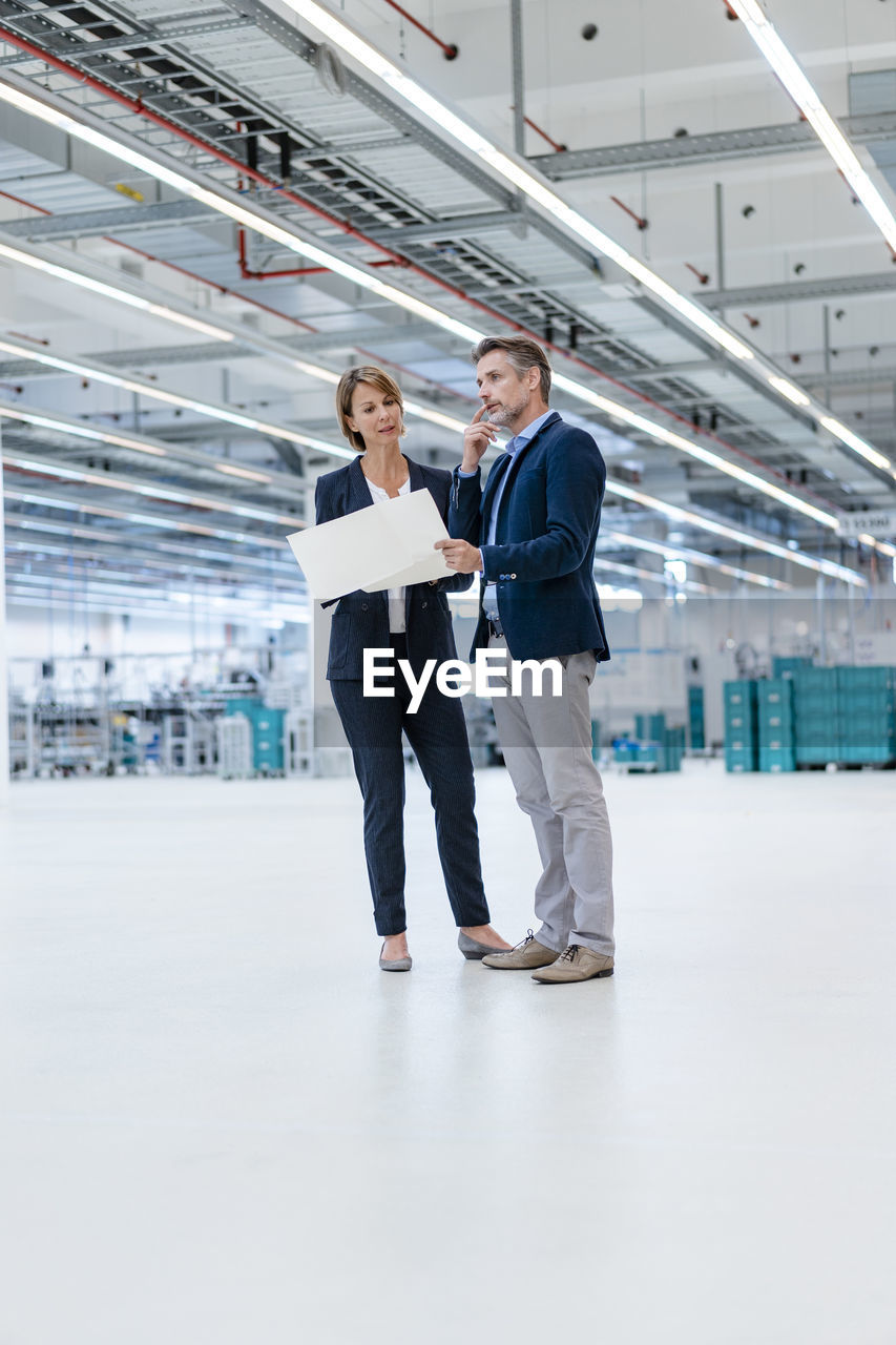 Businessman and businesswoman discussing plan in a factory hall