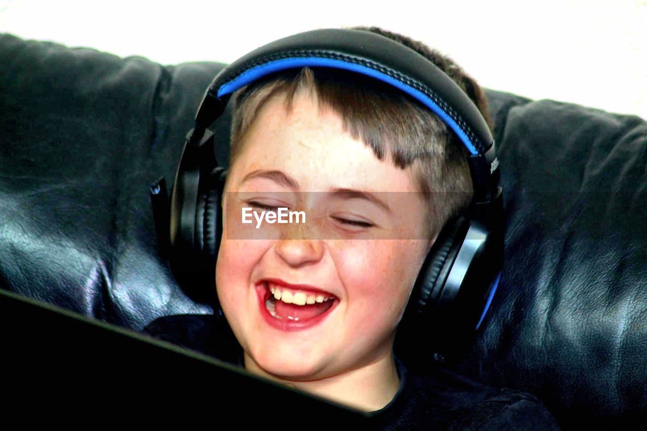 Happy cute boy listening music through headphones on sofa at home