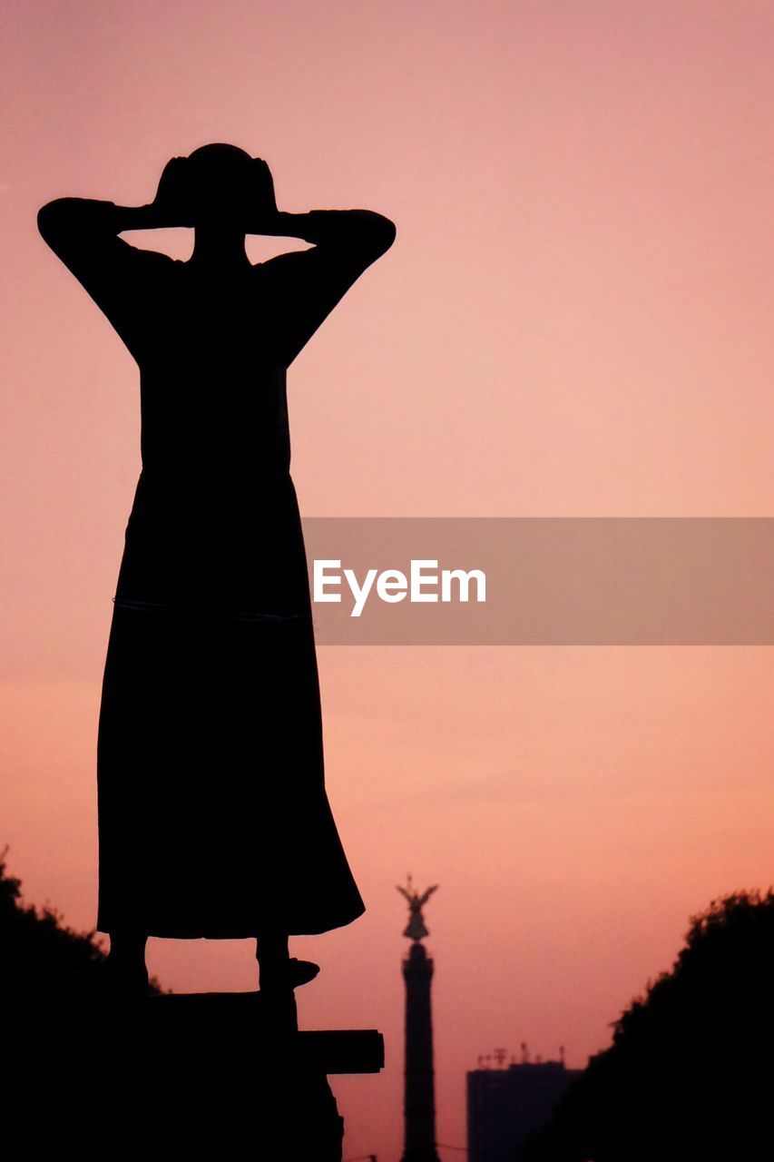 Silhouette of woman statue standing against sky during sunset shouting 