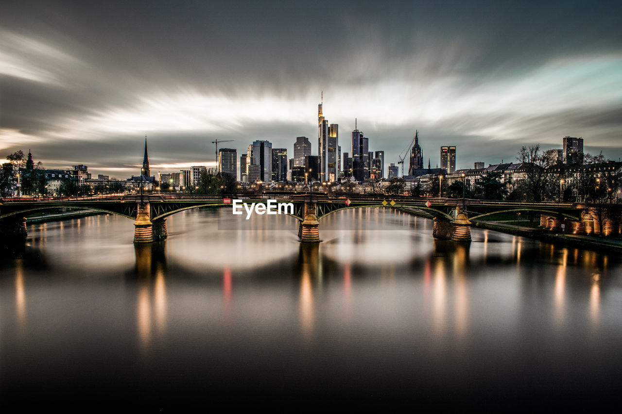 Illuminated buildings by river against sky in city in frankfurt, germany 