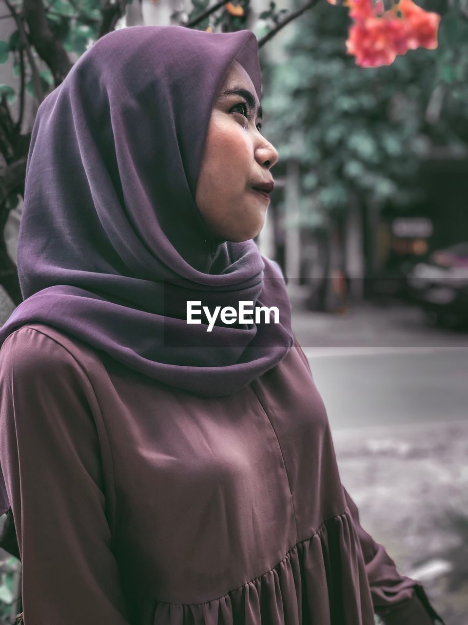 Smiling young woman looking away while standing against trees