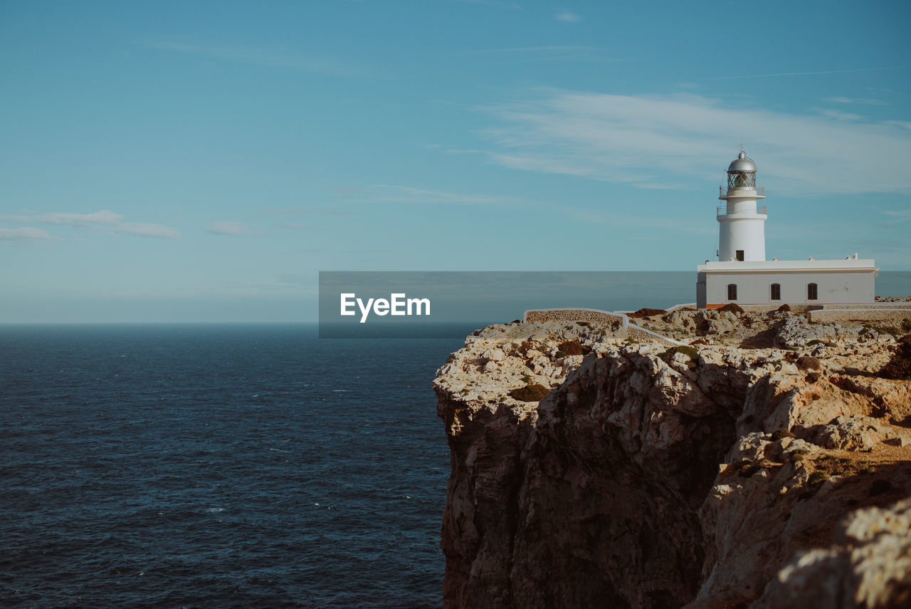 Lighthouse on cliff by sea against sky