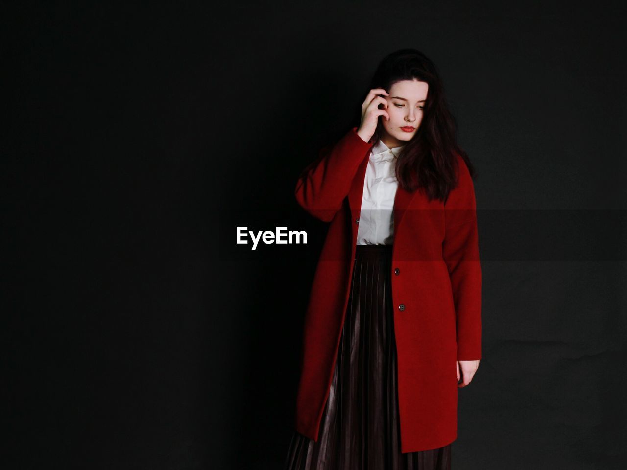 Young woman wearing red long coat against black background