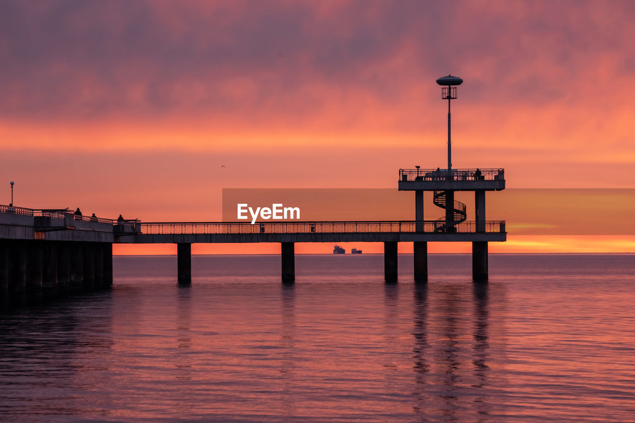 Pier over sea against dramatic sky during sunset