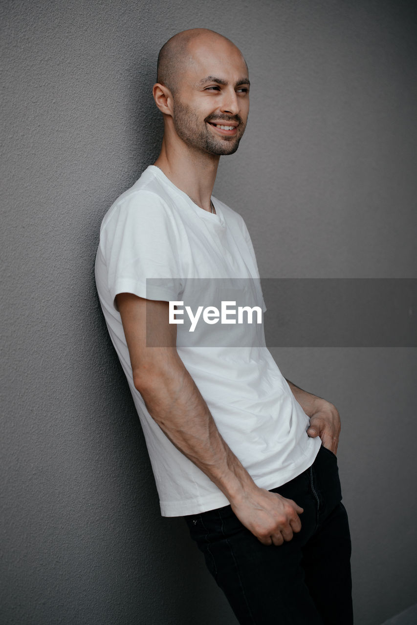 Images of a smiling bald man in his thirties against a gray wall. vertical arrangement