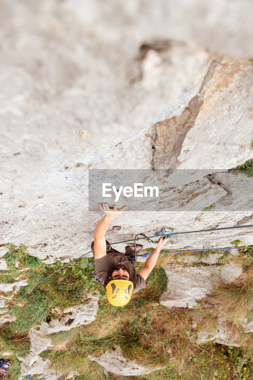 Sportive male alpinist climbing on sheer cliff in summer day