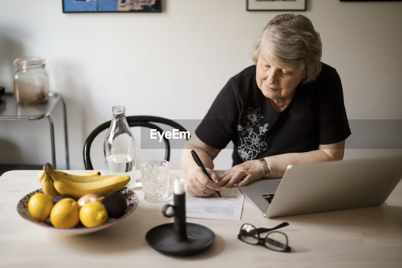 Senior woman checking for bills while using laptop at table