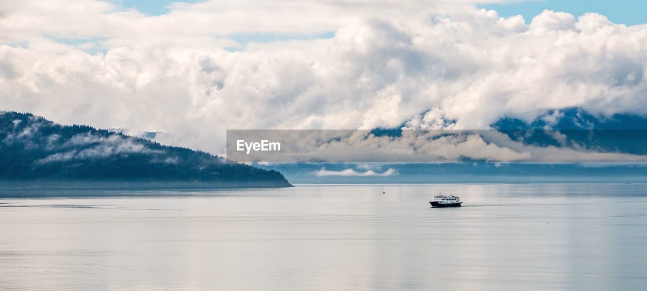 Ship sailing in sea against cloudy sky