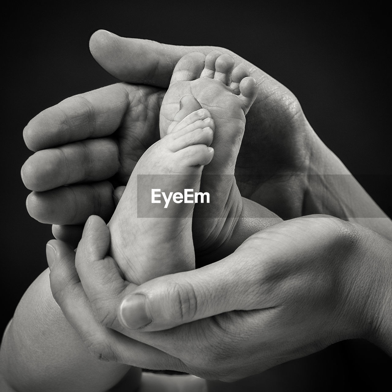 Cropped hands of mother holding baby legs against black background
