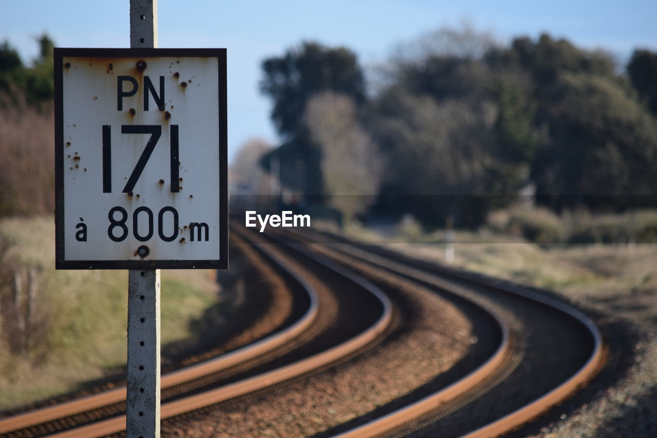 Close-up of road sign by railroad tracks against sky