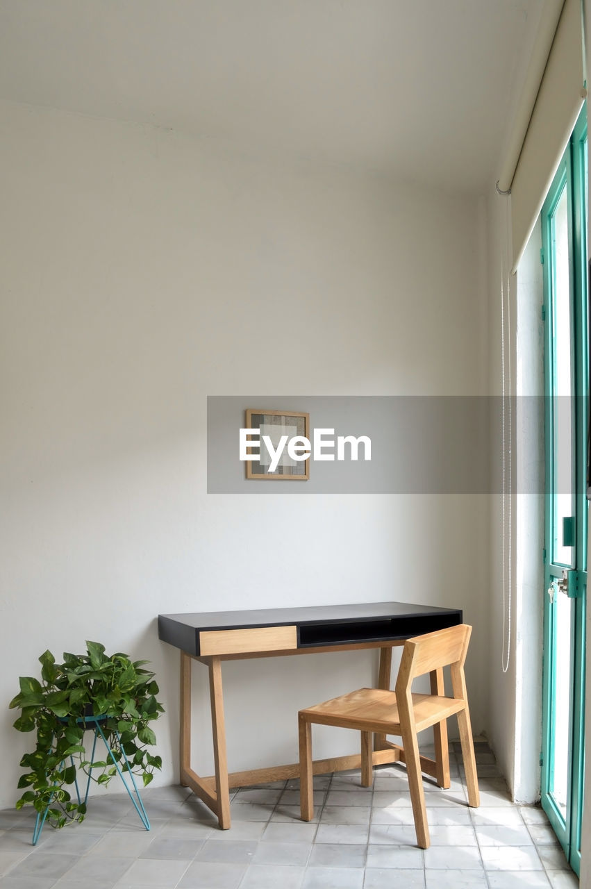 Wooden desk with chair, plants in the room, natural sunlight coming in, pasta tile floor, white 