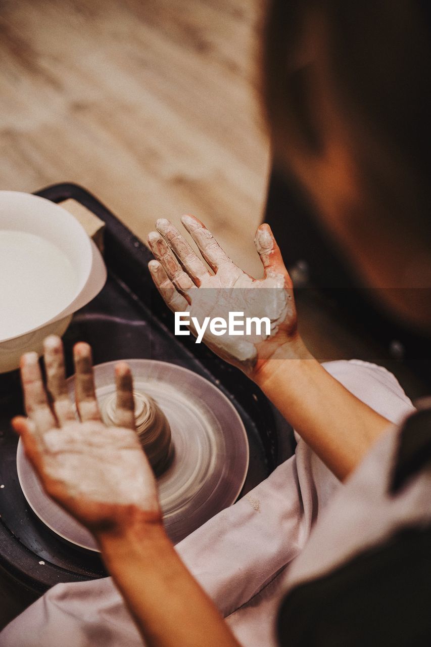 Cropped image of woman with messy hands sitting by pottery wheel