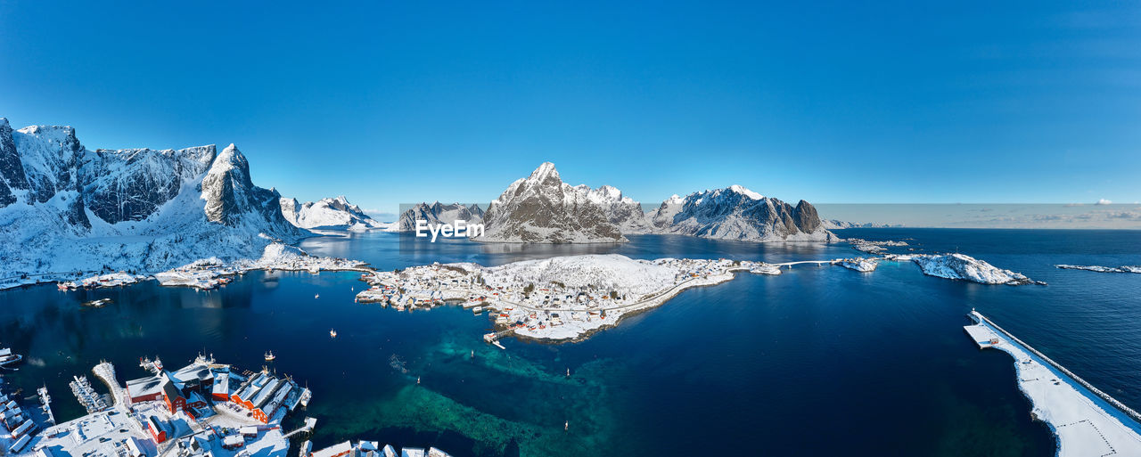 Panaromic aerial shot of isolated fishing valley against clear sky, surrounded by snowy mountains