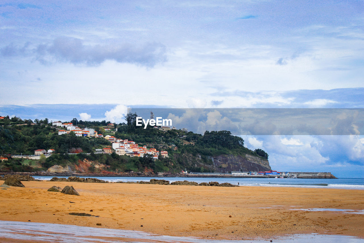 Houses on cliff by beach against sky