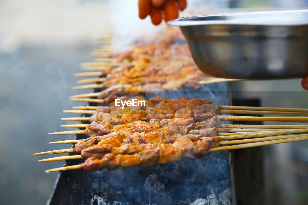 Cropped hand of person cooking meat on barbecue grill