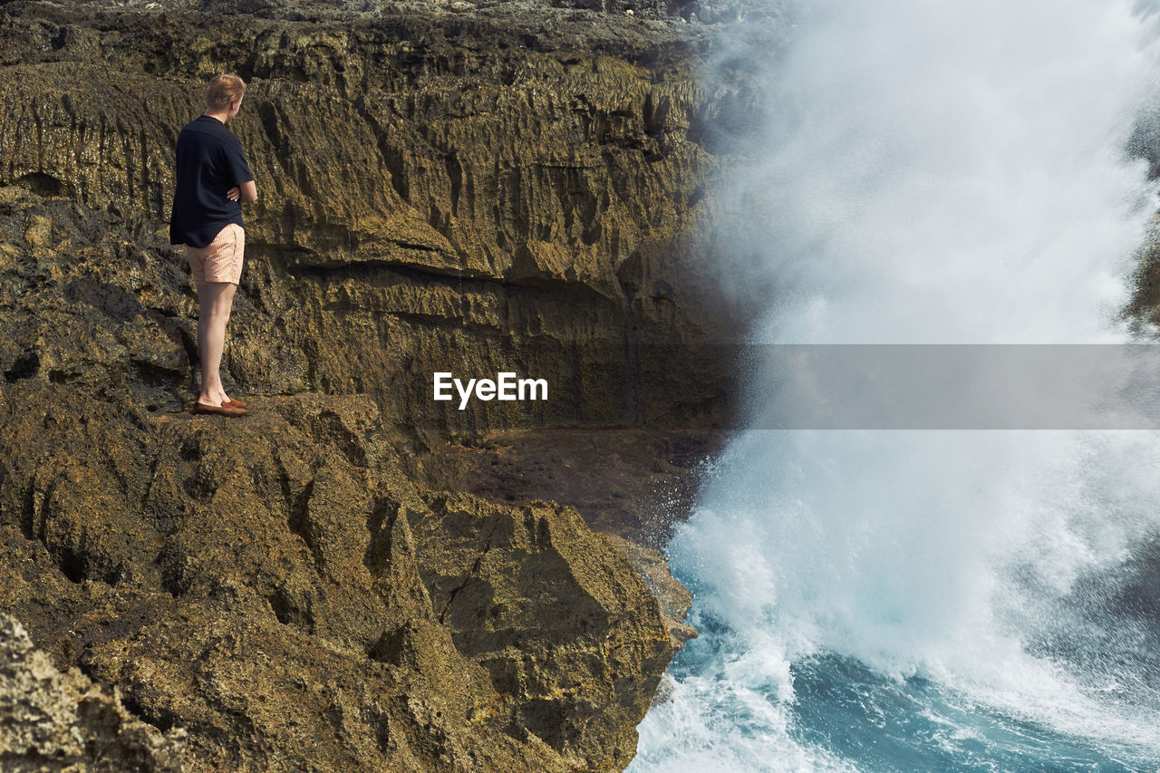 Rear view of woman standing on cliff by sea