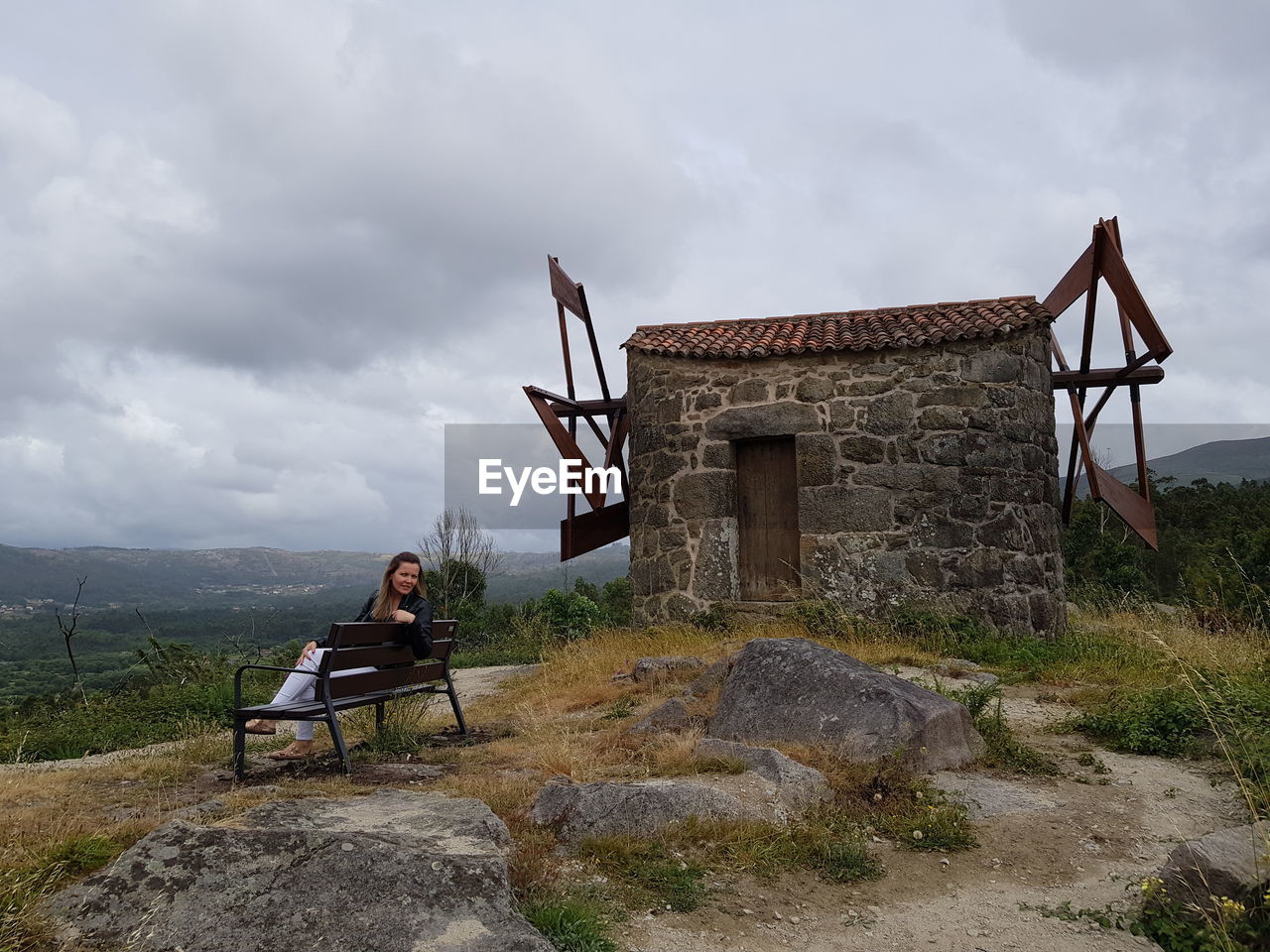 YOUNG WOMAN SITTING ON ROCK AGAINST BUILDING