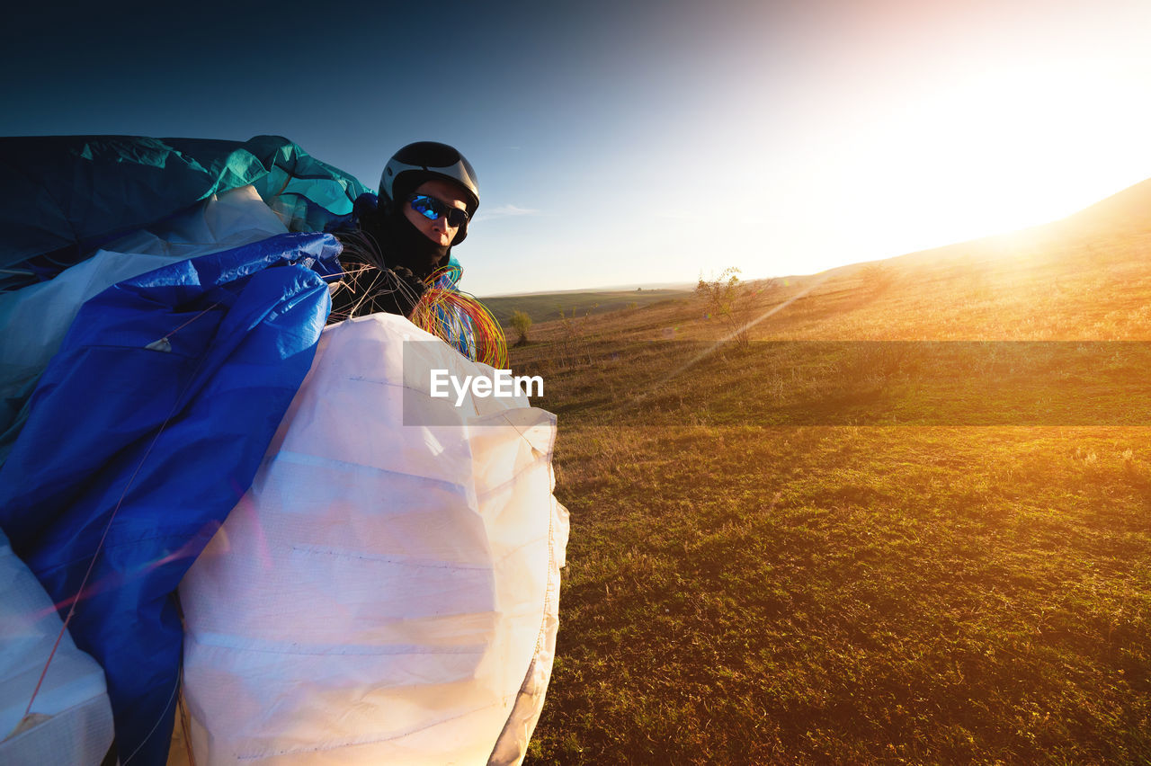 A young male paraglider at sunset in the mountains collects his paraglider to take it to the