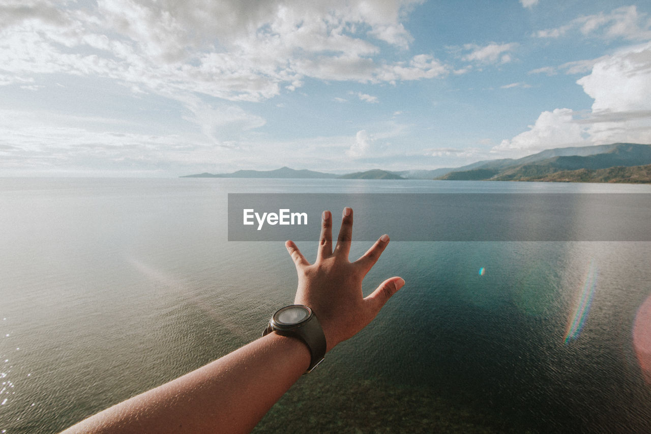 Close-up of hand by sea against cloudy sky