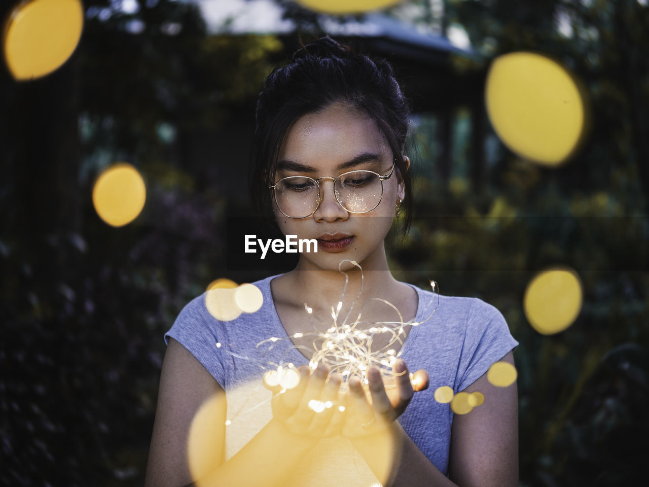 Young woman holding string lights standing outdoors