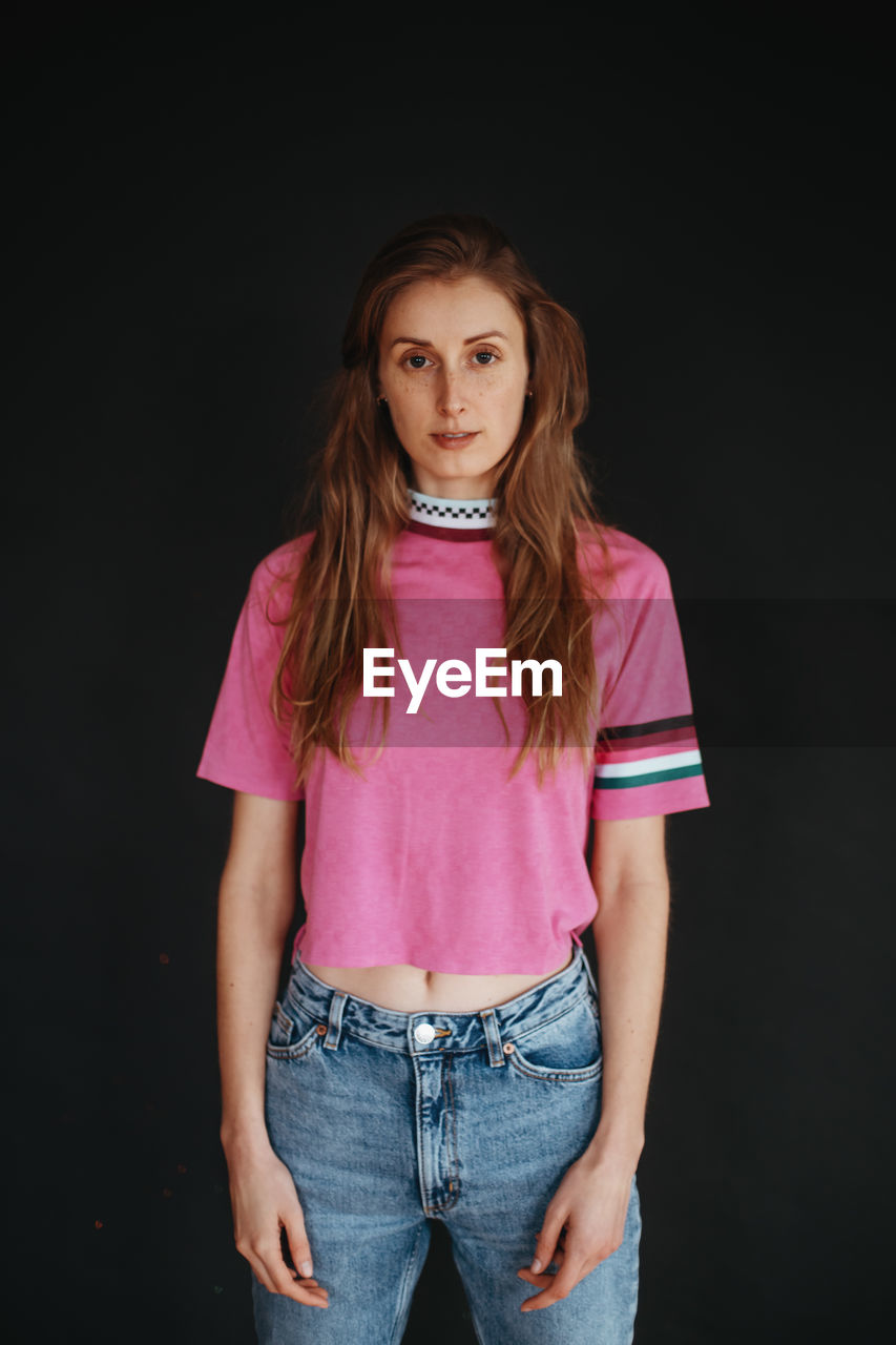 Portrait of young woman standing against black background