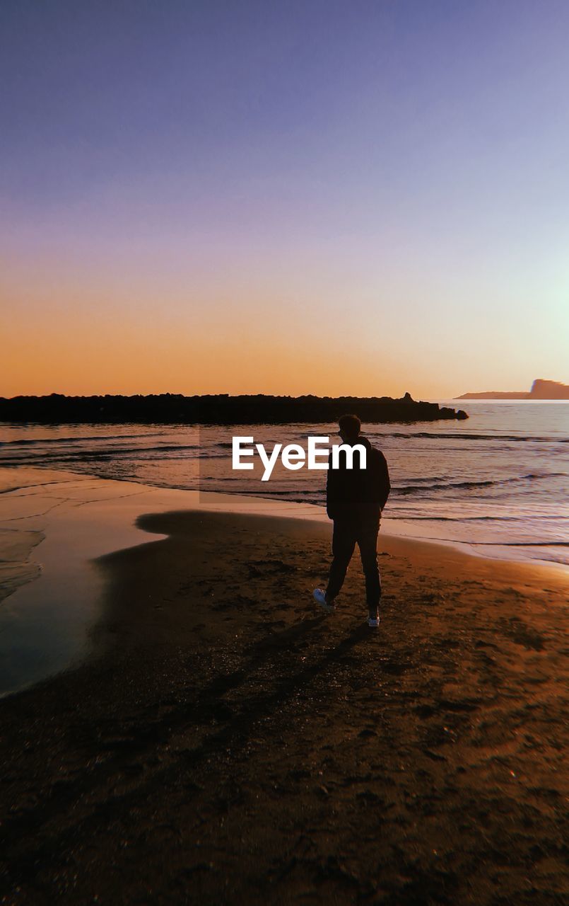 Rear view of silhouette man standing on beach during sunset