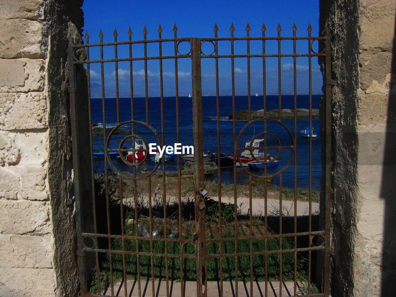 Boats moored in sea seen through closed metallic gate