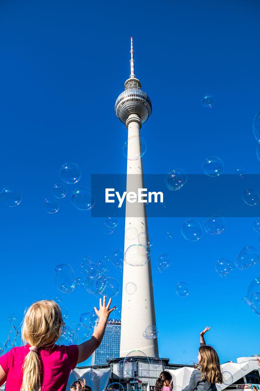 Low angle view of girls playing with bubbles against fernsehturm