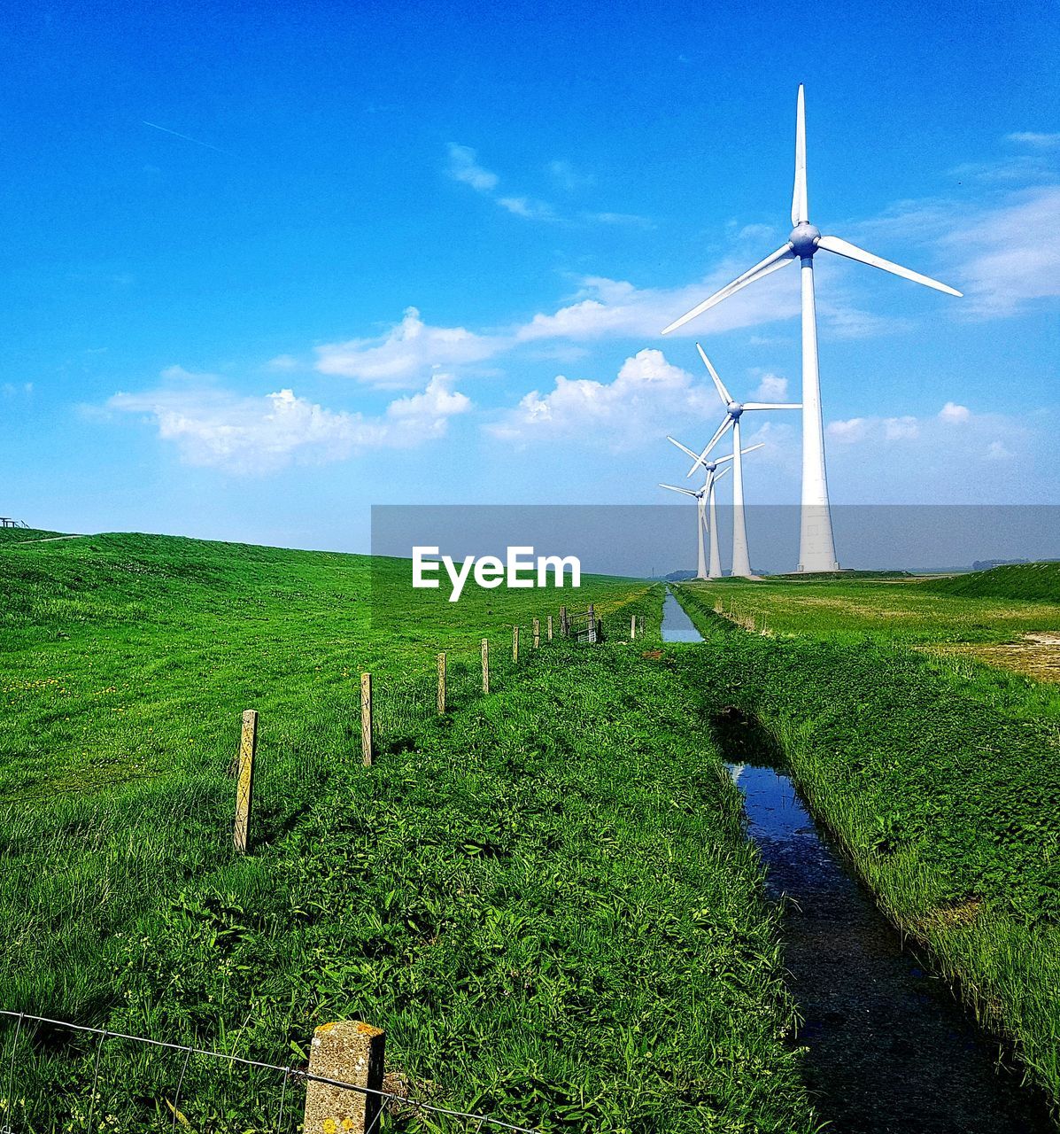 Scenic view of agricultural field against sky with wind turbine as backdrop. 