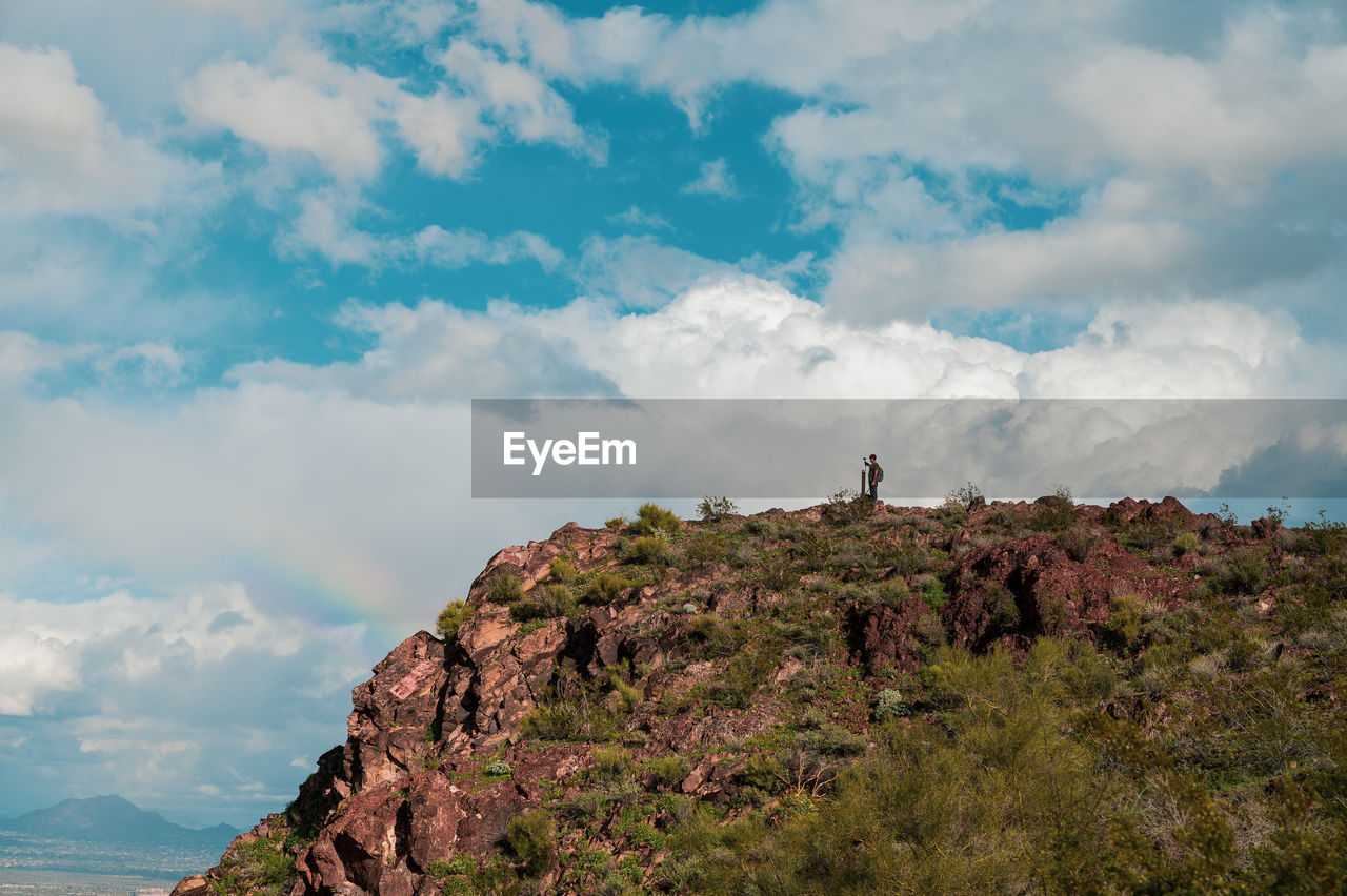 Distant of man standing on mountain against cloudy sky