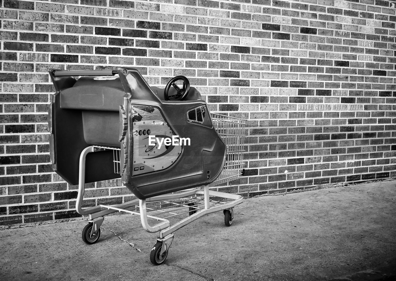 Broken toy car on shopping cart against brick wall