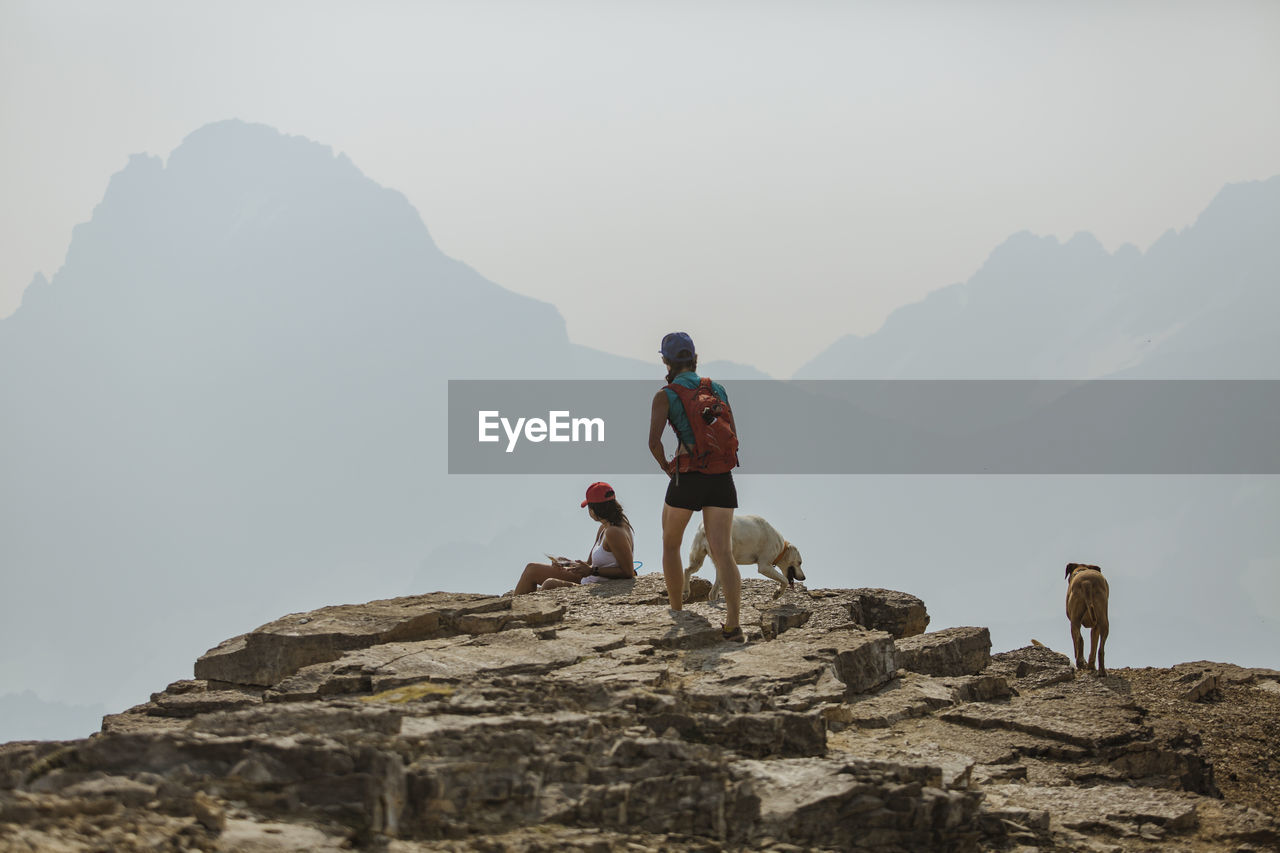 Female hikers with dogs on mountain against sky