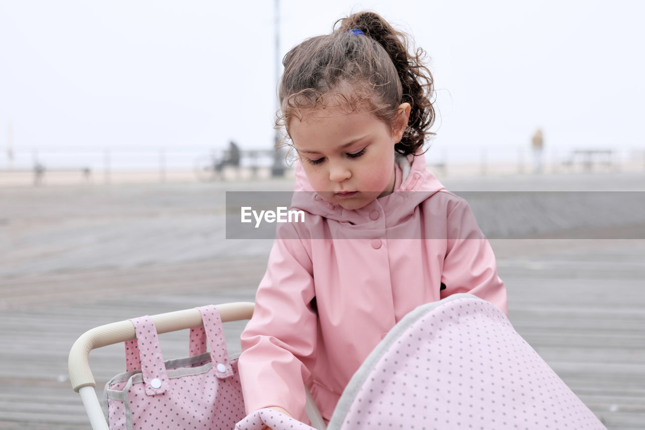 Young girl playing with her toy stroller on the boardwalk