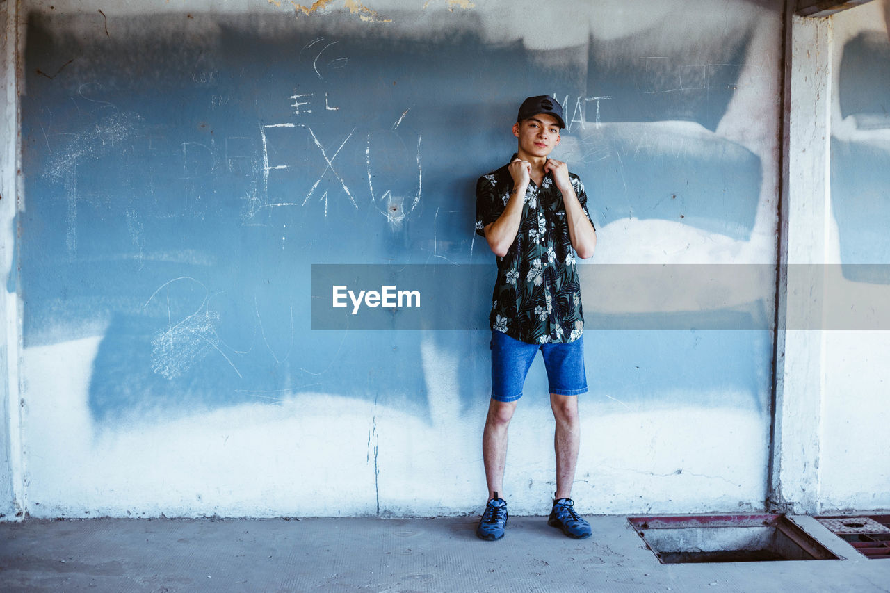 Portrait of young man standing against weathered wall