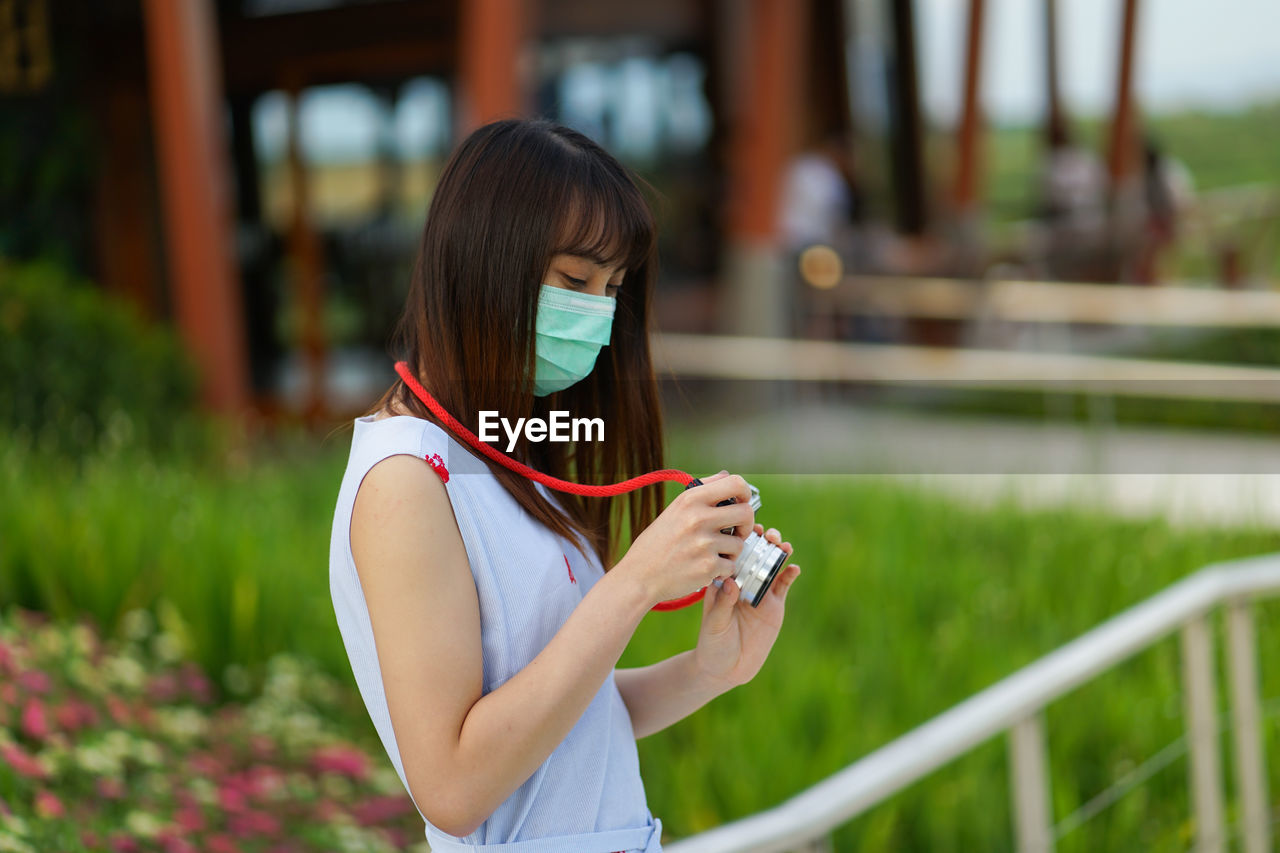 MIDSECTION OF WOMAN HOLDING MOBILE PHONE WHILE STANDING ON CAMERA