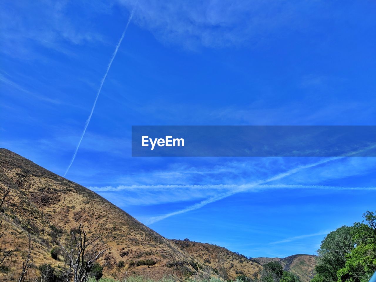 Low angle view of vapor trails against blue sky and mountains