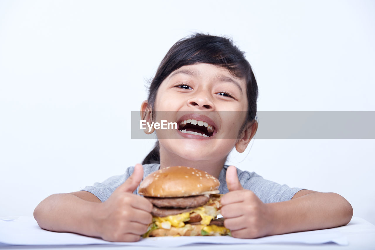 eating, food, child, childhood, unhealthy eating, white background, fast food, food and drink, one person, portrait, hamburger, happiness, sandwich, studio shot, person, smiling, emotion, meal, cute, snack, indoors, fun, mouth open, bread, men, cheerful, human mouth, hungry, cut out, front view, lunch, meat, toddler, enjoyment, holding, positive emotion, fast food restaurant, lifestyles, looking at camera, facial expression, casual clothing, biting, take out food, headshot, joy, baked, looking, chivito, human face